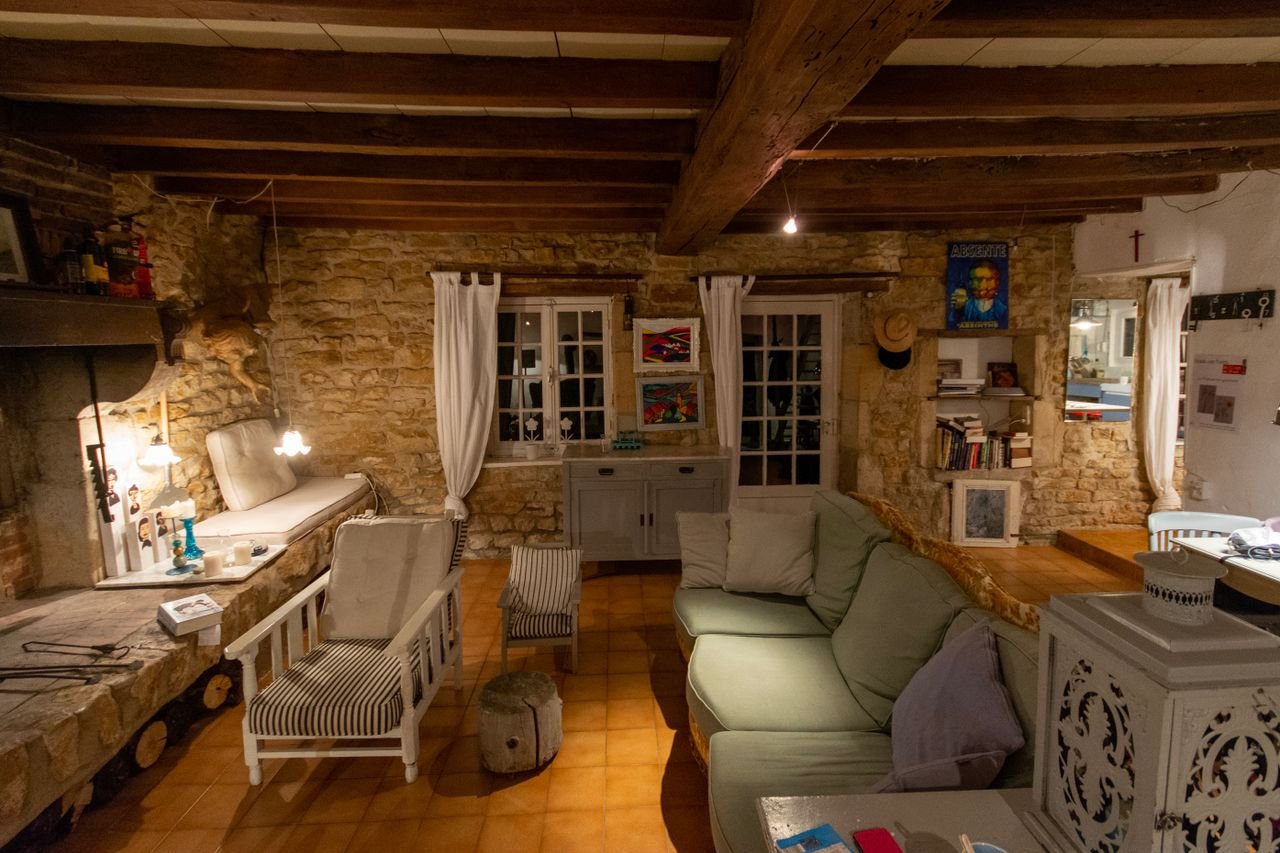 Warm rustic living room with stone walls, wooden beams, armchairs, and sofa creating a cozy ambiance.