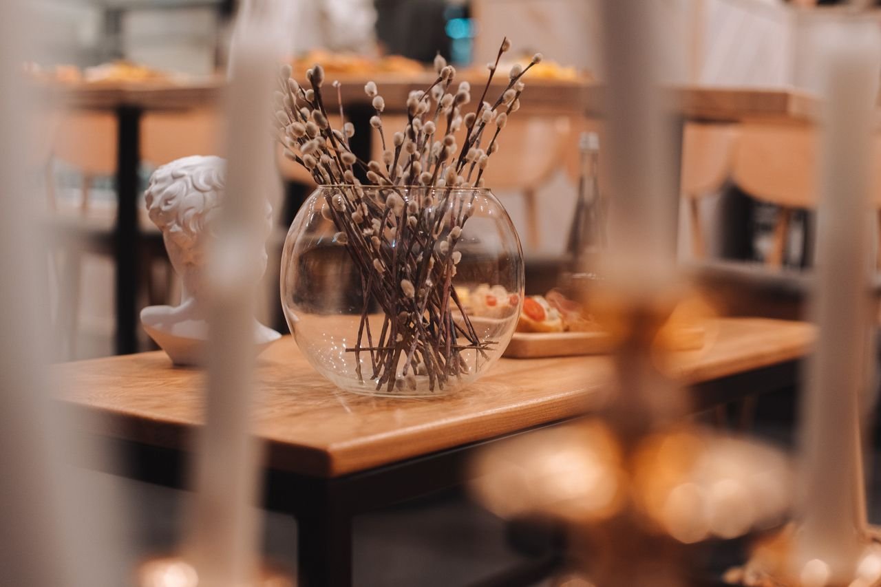 A sophisticated table setting featuring a glass vase with pussy willow branches and a decorative bust.